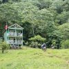 Un grupo de persoas facendo sendeirismo e nadando preto dunha pequena casa nunha ladeira.